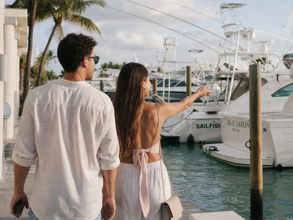 Two guests walking a Miami marina dock, pointing out charter boats