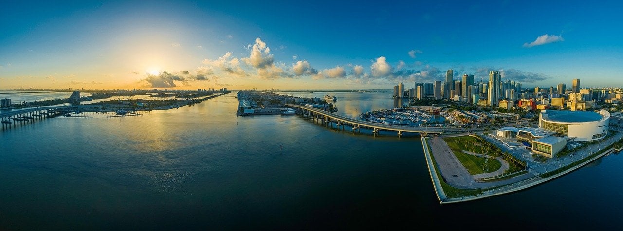 An aerial view of Miami's waterfront and downtown skyline at golden hour, the backdrop of a Star Island yacht tour.