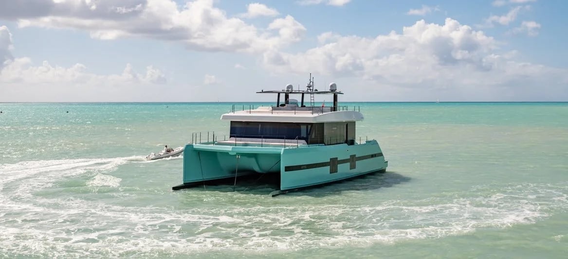 Turquoise catamaran with dual hulls anchored in shallow Caribbean waters under bright blue skies